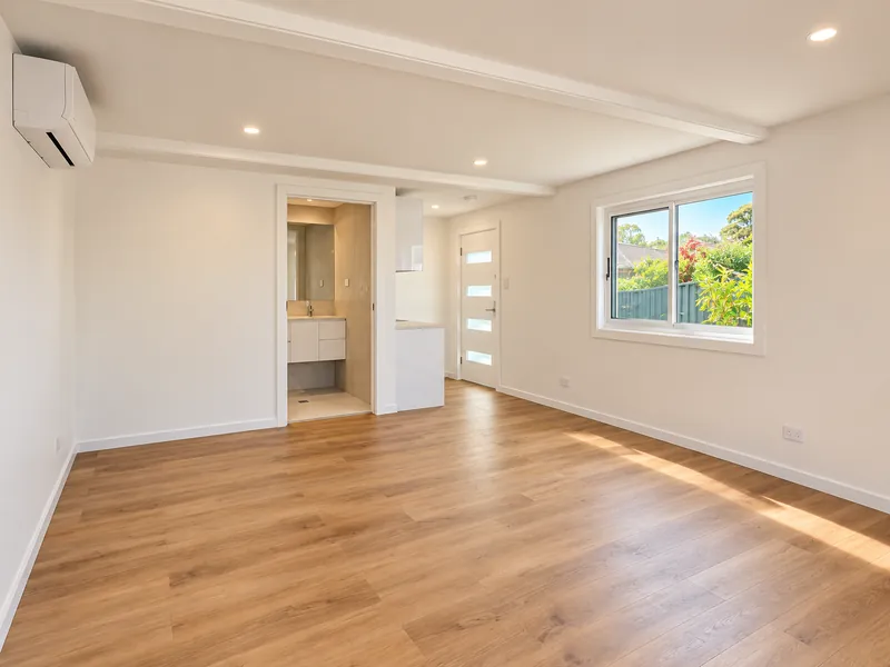 Bright converted living space with timber flooring and a garden-facing window