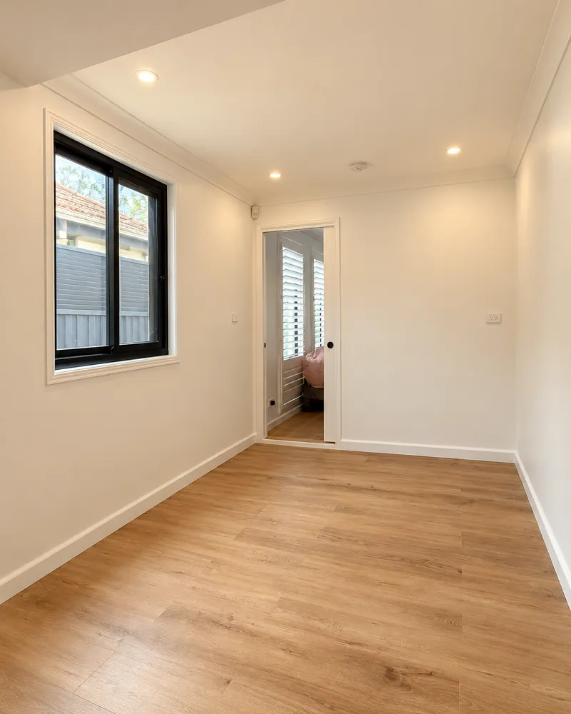 Converted room with timber flooring, a black-framed window and an adjoining room