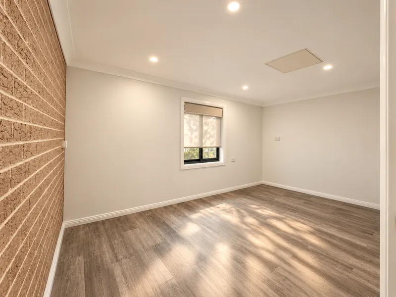 Empty converted room with timber-look flooring, a brick feature wall and a sunlit window
